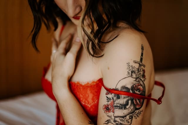 photo boudoir et tatouage. Le visage de la jeune femme est éclairé par une lumière douce et chaleureuse, mettant en valeur la texture de sa peau, et accentuant les ombres délicates qui soulignent ses traits. Le photographe a choisi une ouverture de diaphragme assez large, créant ainsi un arrière-plan flou et une profondeur de champ réduite. Cette technique permet de concentrer l'attention du spectateur sur le sujet principal et de renforcer l'impact émotionnel de l'image.

Les tons chauds de la photographie, allant du beige au brun, en passant par des nuances d'orange et de doré, créent une atmosphère apaisante et intime. L'utilisation d'une composition centrée met en avant la symétrie du visage de la jeune femme, apportant une harmonie visuelle à l'image.